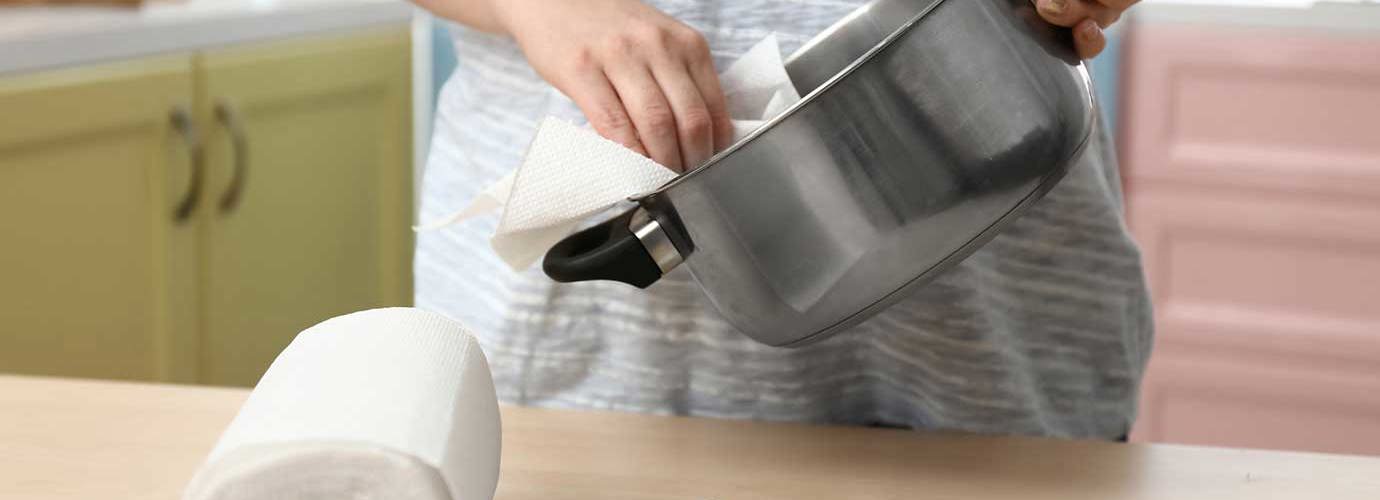 Een persoon naast het aanrecht en maakt een pot schoon met een vel keukenpapier 