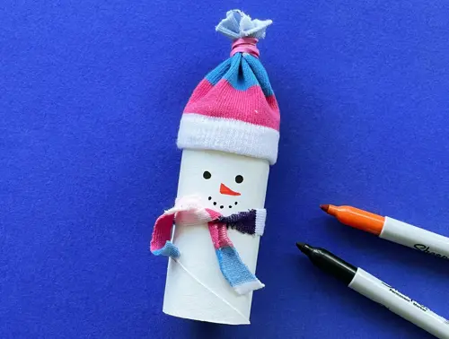 PVA-lijm en gekleurde knopen liggen naast de sneeuwpop, en onder de gestreepte sjaal zijn 3 knopen in een lijn gelijmd.