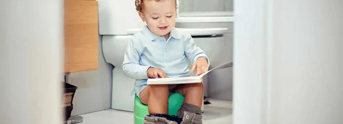 Een kleine jongen zit op een potje te kijken naar een boek op zijn schoot