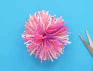 Een pompon gemaakt met verschillende tinten roze wol, met een schaar aan de zijkant.
