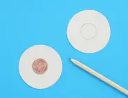Twee kartonnen uitgeknipte cirkels op een blauw oppervlak met een munt in het midden en een potlood aan de zijkant.