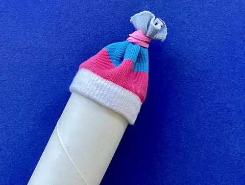 De gestreepte sok is dichtgebonden met een roze elastiekje, die de 'pompon' van de muts vormt.