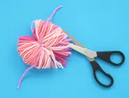 Een zwarte schaar knipte de buitenste uiteinden van de lus in strengen, die allemaal nog steeds vastzitten aan het roze wollen koordje in het midden.