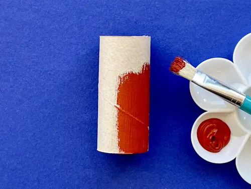 Deels bruin geverfde wc-rol met een kunststof verfpalet met bruine verf en een penseel ernaast.