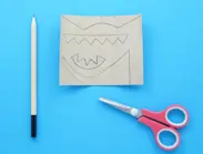 Opengeknipte wc-rolkoker met dinosaurusstekels en -staart erop getekend en een schaar en potlood erbij.