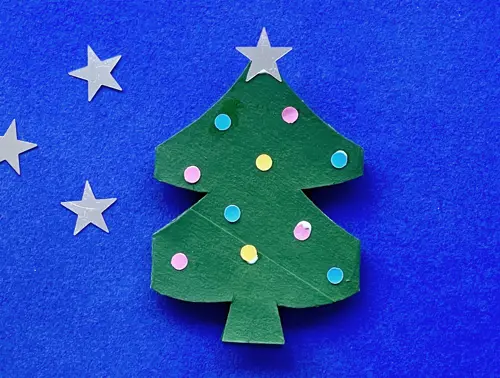 Zilveren sterretjes liggen links van de kartonnen kerstboom, waarop een ster gelijmd is als piek.