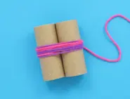 Twee wc-rolletjes naast elkaar, in het midden omwikkeld met roze en paarse wol.