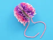 Een roze wollen pompon met karton in het midden, samengebonden met een roze wollen draadje.