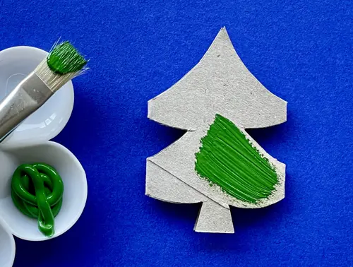 Een van de kerstbomen, half groen geverfd, ligt naast een penseel en groene verf.