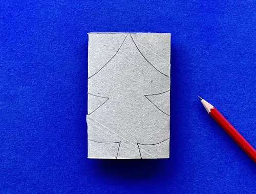 Geplette kartonnen toiletrolkoker op een blauwe achtergrond met een potloodtekening van een kerstboom om uit te knippen.