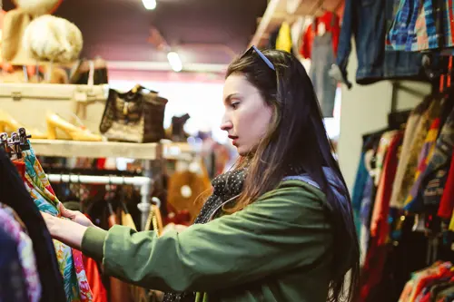 Een vrouw winkelt alleen in een kringloopwinkel en inspecteert kledingrekken.